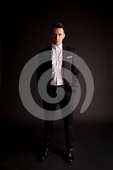 A confident elegant handsome young man standing in front of a black background in a studio wearing a nice suit