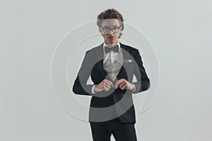 Confident elegant man with eyeglasses unbuttoning black tuxedo