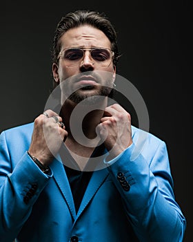 confident elegant man with glasses looking forward and adjusting shirt collar