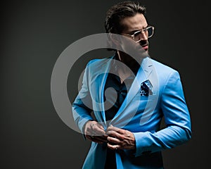 confident elegant man with glasses looking to side and adjusting blue suit