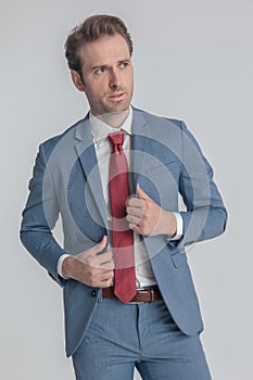 Confident elegant man looking to side and fixing blue suit