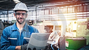 Confident engineer in blue jumpsuit holding laptop computer in a warehouse.