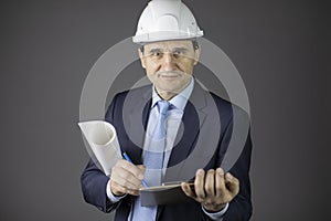 Confident engineer in hard hat with clipboard and blueprint roll looks at camera