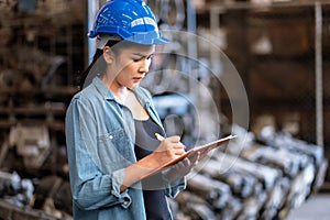 Confident engineer woman workers wear a safety helmet and standing in the automotive spare parts warehouse. Writing on the