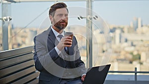 Confident executive sipping coffee on glass terrace. Handsome business browsing