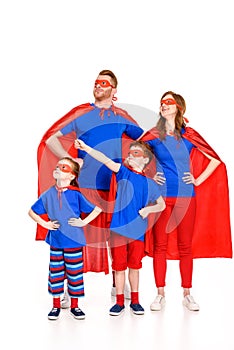 confident family of superheroes in masks and cloaks standing with hands on waist and looking away