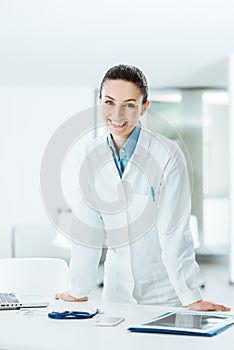 Confident female doctor leaning on desk