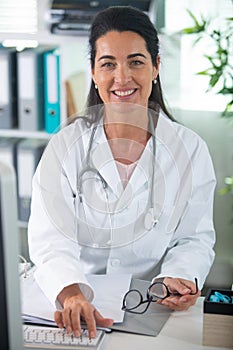 confident female doctor sitting at office desk and smiling