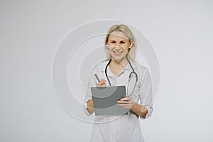 Confident female doctor in white medical coat and stethoscope looking calm on clipboard with patient s medical history
