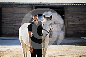 Confident female jockey standing by white horse at barn