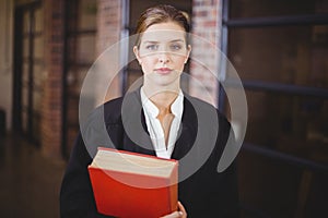 Confident female lawyer with book standing in office