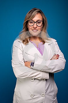 Confident female nurse dressed in beige colored coat wearing eyeglasses with arms crossed. Positive person