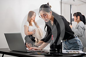 A confident female photographer checking images on her laptop, working with her team in the studio