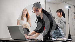 A confident female photographer checking images on her laptop, working with her team in the studio