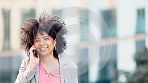 Confident female real estate agent talking on the phone while walking outdoors in the city. A successful African woman