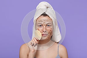 Confident female with scrub on face doing procedures for cleansing and peeling, holding sponge near face, looks at camera, being