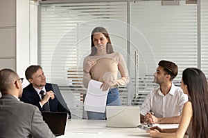 Confident female speaker standing, explaining project results to multiracial colleagues.