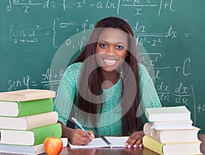 Confident female teacher writing in book at classroom desk