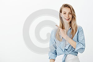 Confident feminine female shop assitant in stylish clothes, raising index finger and pointing at upper left cornern