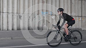 Confident fit focused cyclist riding a bicycle wearing helmet, black outfit and sunglasses. Bearded bike rider pedaling bicycle. S
