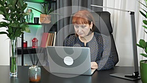 Confident focused woman is sitting at her modern office in front of laptop computer. Businesswoman is typing on notebook keyboard