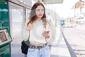 Confident girl walking along a tram stop holds a mobile phone photo