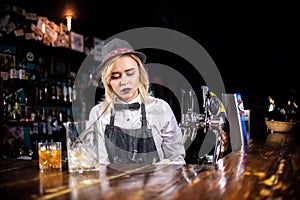 Confident girl bartender pouring fresh alcoholic drink into the glasses at bar