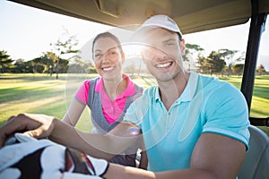 Confident golfer couple sitting in golf bugggy