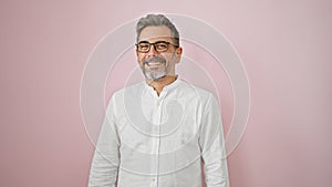 Confident, grey-haired hispanic man flaunting a charming smile, wearing glasses, standing over an isolated pink background,