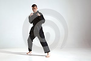 Confident guy in black kimono fighter posing in karate stance on studio background with copy space, mix fight concept