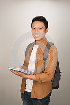 Confident handsome Asian student holding books and smiling at camera