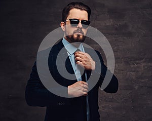 Confident handsome fashionable middle-aged man with beard and hairstyle dressed in an elegant formal suit and sunglasses