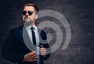 Confident handsome fashionable middle-aged man with beard and hairstyle dressed in an elegant formal suit and sunglasses