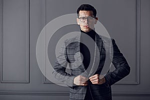 Confident,handsome man of affairs in black eyeglasses, black turtleneck and gray plaid jacket looks serious at camera.