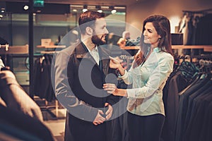 Confident handsome man with beard choosing a coat in a suit shop.