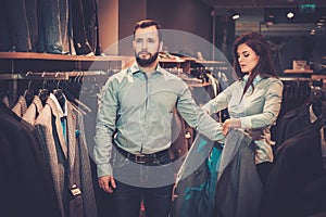 Confident handsome man with beard choosing a jacket in a suit shop.