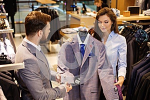 Confident handsome man with beard choosing a jacket in a suit shop.