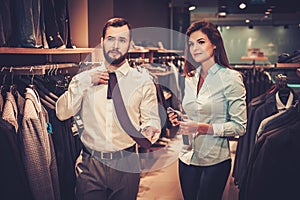 Confident handsome man with beard choosing a tie in a suit shop.