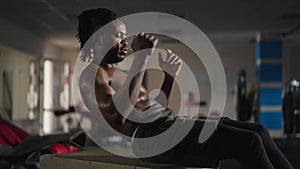 Confident handsome sportsman training belly press exercising in gym indoors. Portrait of African American motivated