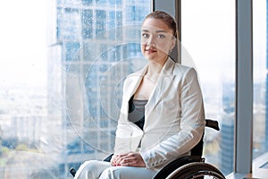 Confident happy businesswoman in wheelchair against the background of a panoramic window overlooking the skyscrapers and