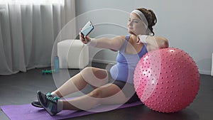 Confident happy obese woman making selfie on smartphone during home workout