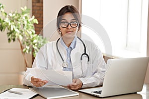 Confident indian female doctor wear white coat looking at camera at work.