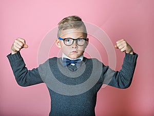 Confident kid boy shows muscles. Sport child boy showing his hand biceps muscles strength. School pupil in glasses. Nerd