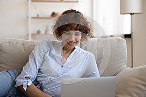 Confident lady recline on couch engaged in chatting by laptop photo