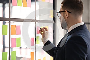 Confident leader wearing glasses writing tasks on sticky papers