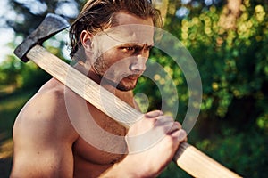 Confident look. Close up portrait of woodsman with axe in hand. Handsome shirtless man with muscular body type is in the