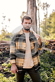 Confident lumberjack works in summer forest. Lumberjack with an ax in the evening.