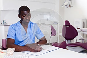 Confident male dentist working with medical records in dental office