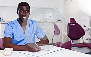 Confident male dentist working with medical records in dental office