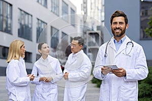 Confident male doctor with tablet and team of medical professionals outdoors